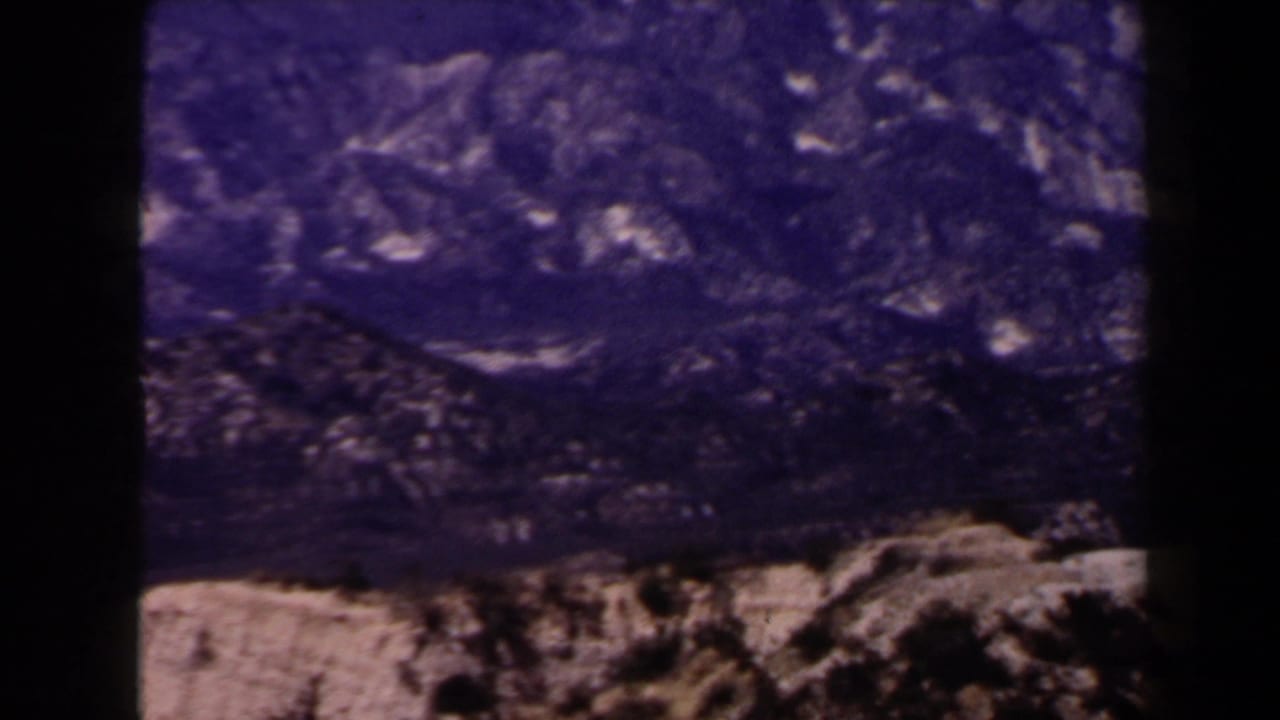 1958 Las Vegas-area 8mm frame showing rugged, treeless rocky mountains under a strong blue-purple cast.