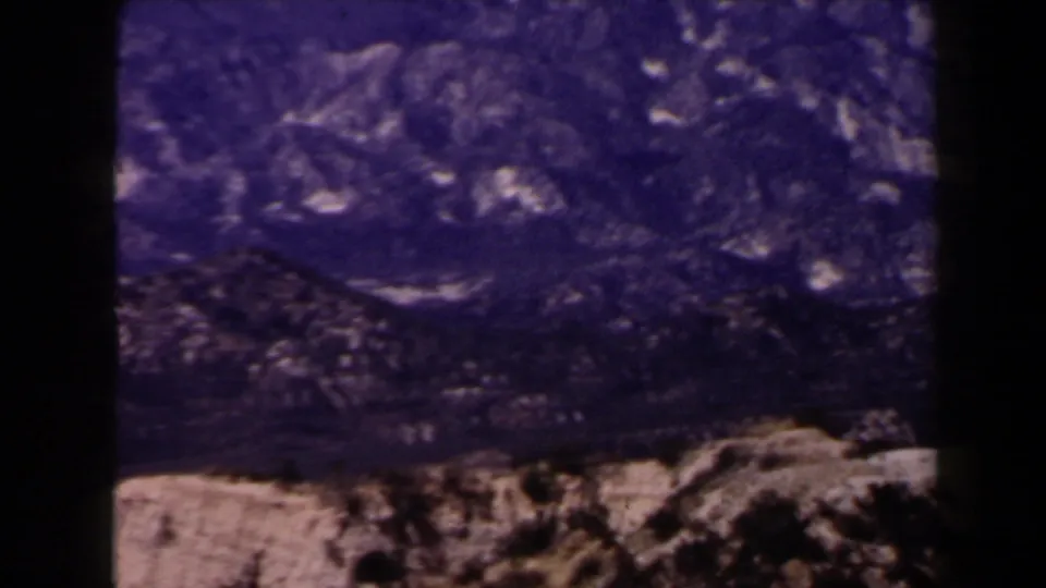 1958 Las Vegas-area 8mm frame showing rugged, treeless rocky mountains under a strong blue-purple cast.
