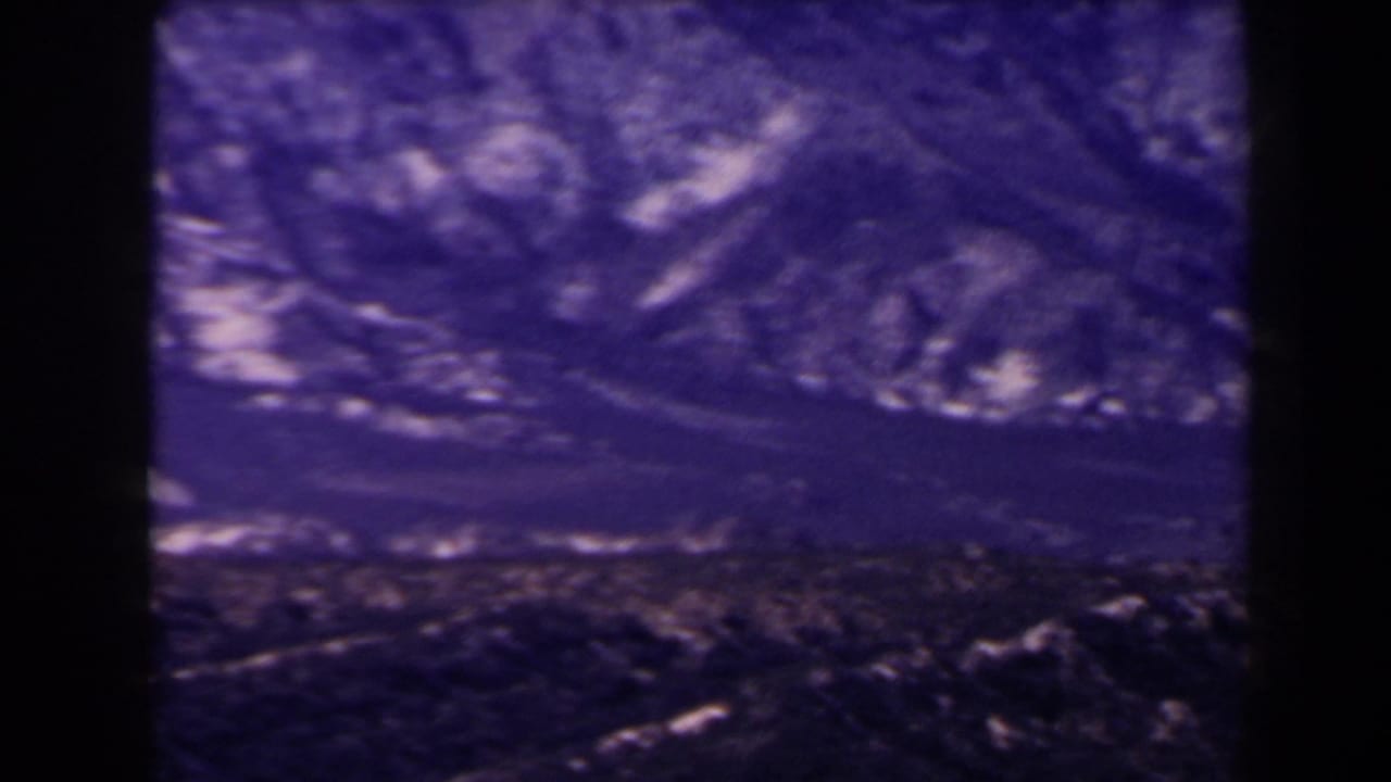 1958 Las Vegas-area home-movie frame with layered rocky ridges and dark arid foreground terrain.