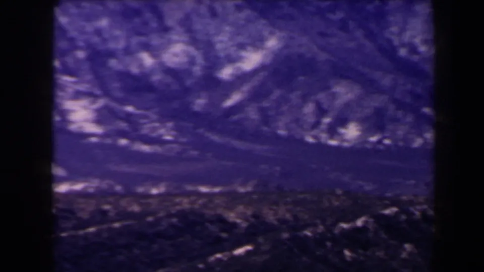 1958 Las Vegas-area home-movie frame with layered rocky ridges and dark arid foreground terrain.