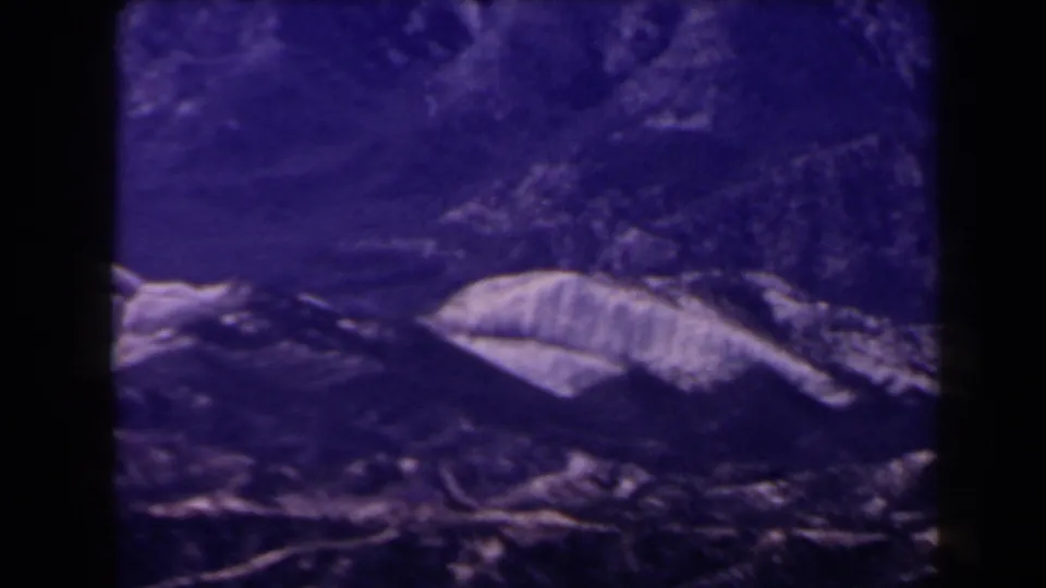 1958 Las Vegas-area 8mm frame showing a soft, purple-cast mountain slope with pale rocky ridges and dark film borders.