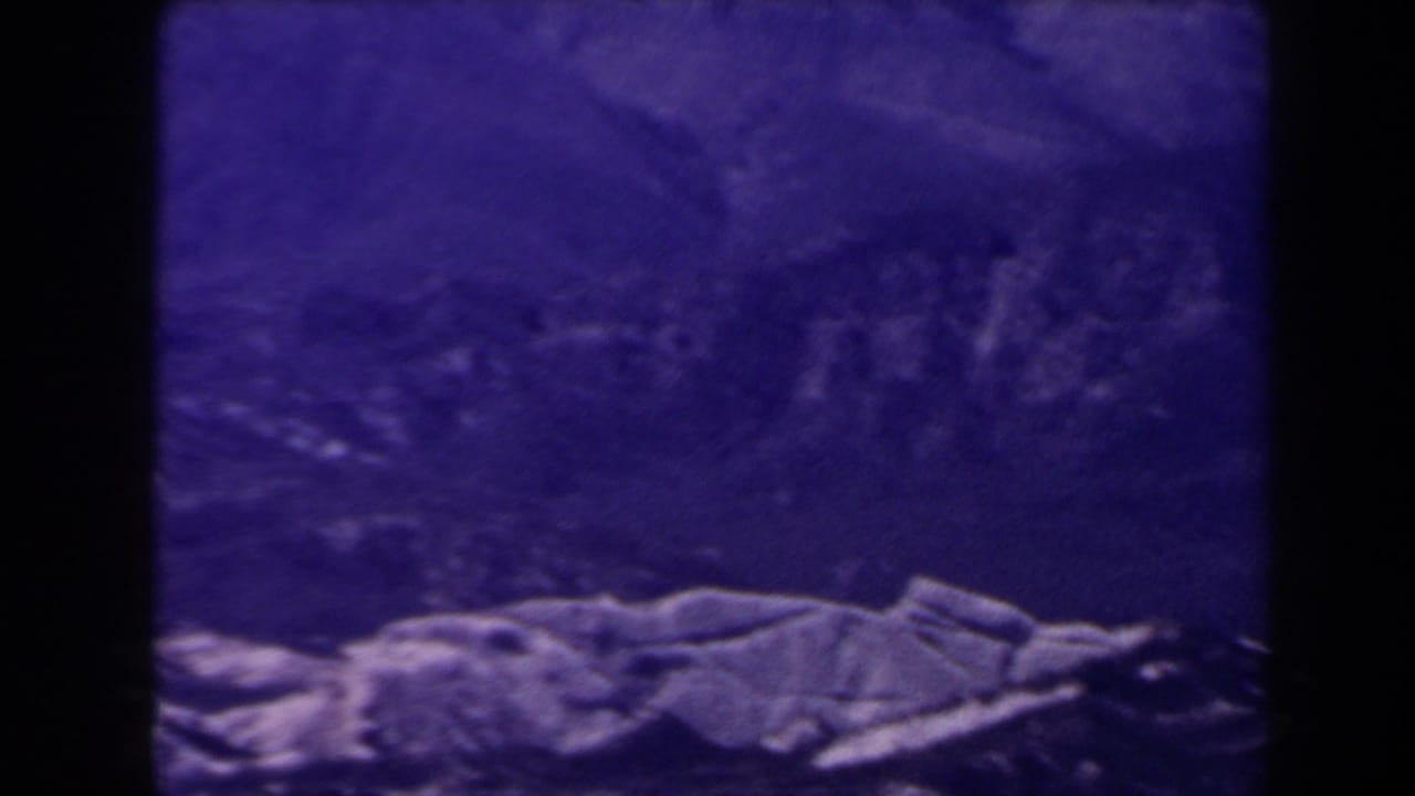 1958 Las Vegas-area home-movie frame with a dark purple mountain backdrop and pale rocky terrain crossing the lower edge.