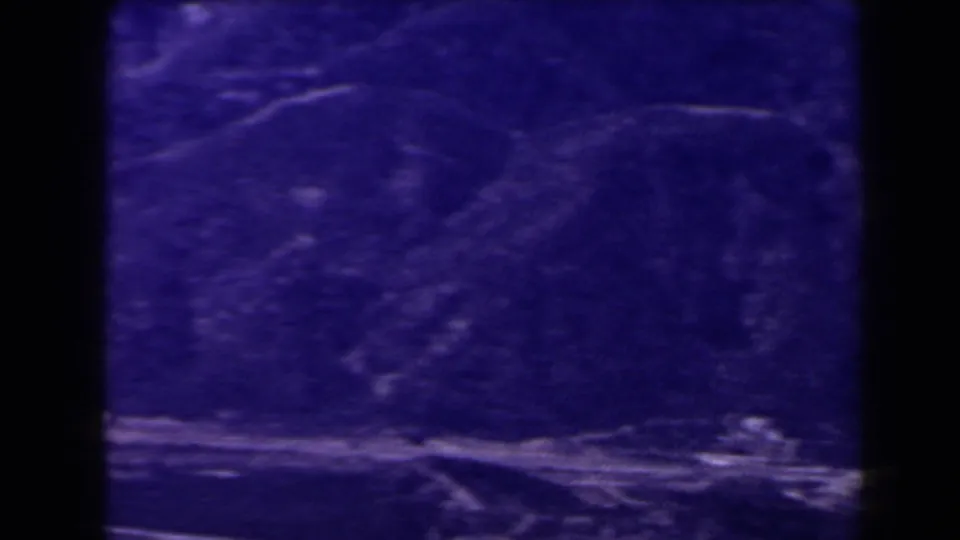 1958 Las Vegas-area 8mm frame with a purple mountain valley, faint path traces, and a pale rocky strip along the lower edge.