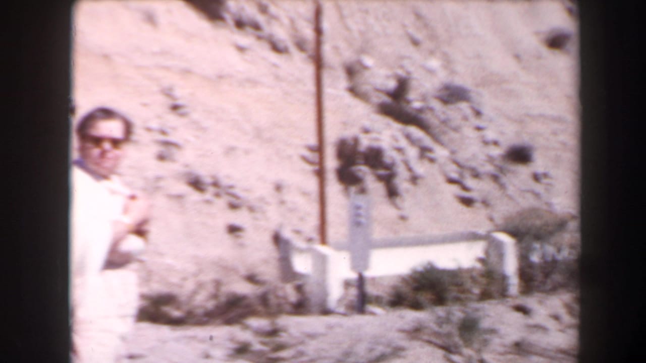 1958 Las Vegas-area home-movie frame showing a man in sunglasses near a pale barrier on a rocky desert roadside.
