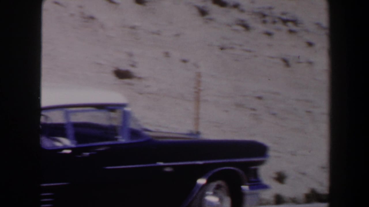 A dark 1950s Cadillac appears in profile along a Las Vegas desert road, with soft 8mm color and chrome details.