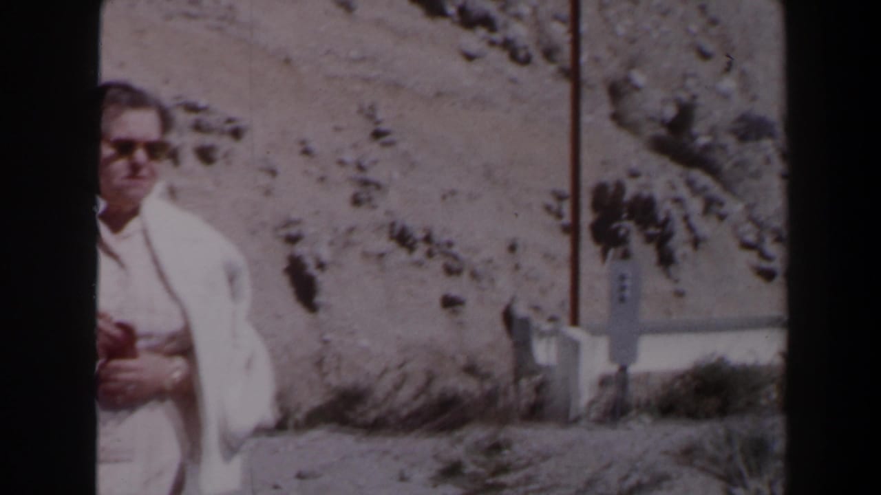 A man in a light shirt and sunglasses holds a camera near a rocky Las Vegas roadside in 1958 home-movie footage.