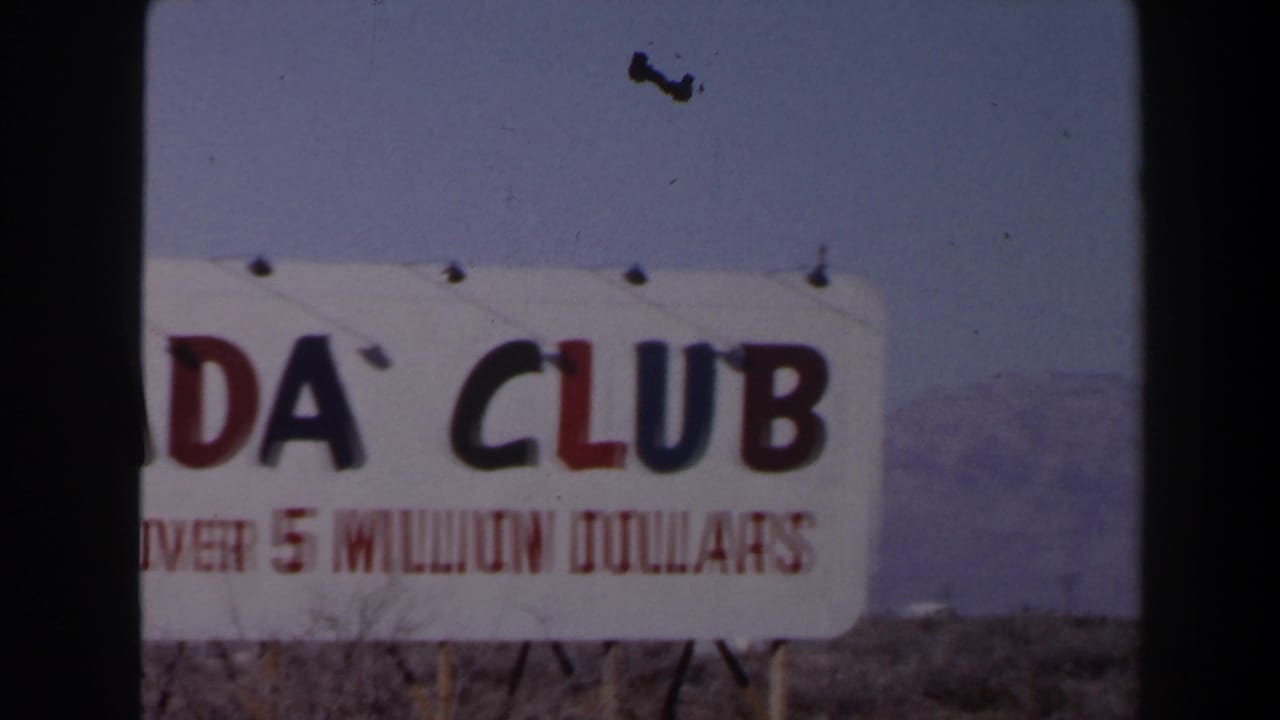 1958 Las Vegas 8mm frame showing a cropped roadside ADA Club sign with “OVER 5 MILLION DOLLARS” partly visible against desert mountains.