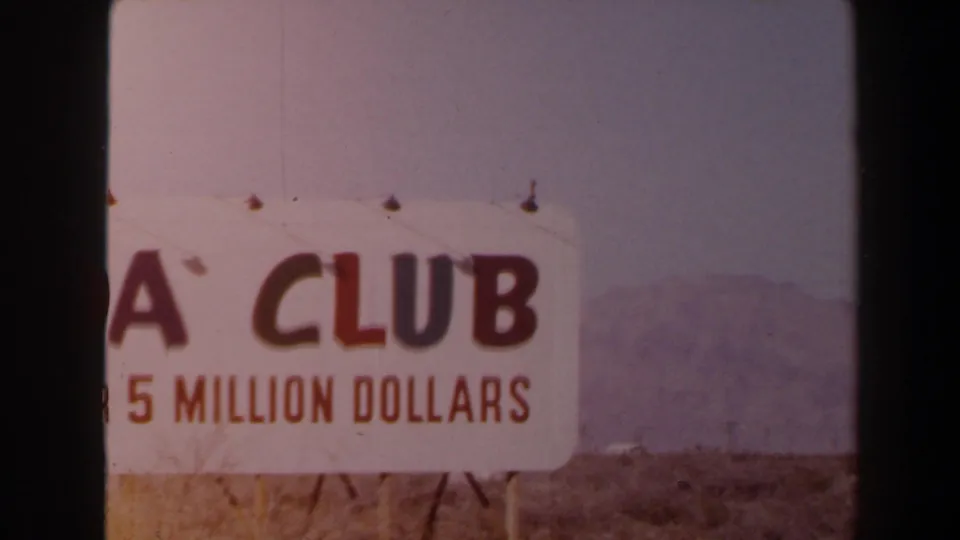 1958 Las Vegas 8mm frame showing a cropped ADA Club sign with “5 MILLION DOLLARS” visible, set before open desert and mountains.