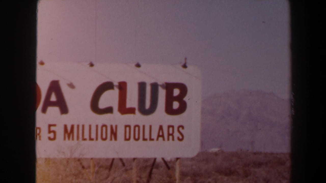 1958 Las Vegas-area 8mm frame showing a cropped white roadside sign with red CLUB lettering, partial 5 MILLION DOLLARS text, dry brush, and distant mountains.