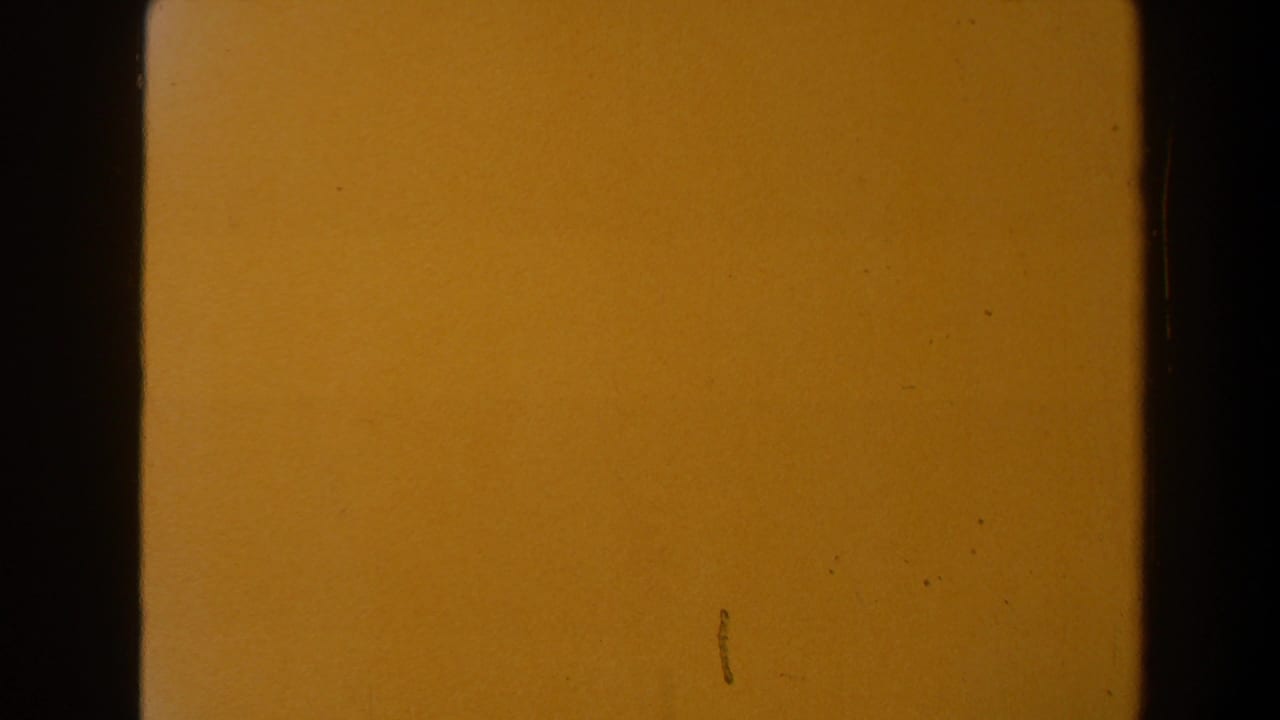 End frame of the 8mm clip fading to a warm orange field with visible grain, small marks, and dark film edge shadows.
