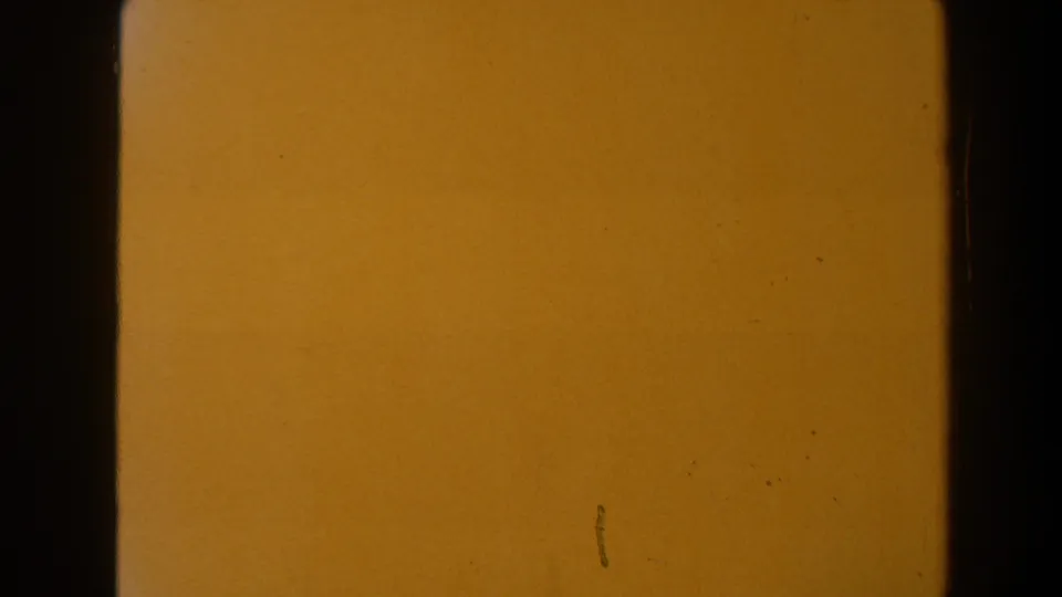 End frame of the 8mm clip fading to a warm orange field with visible grain, small marks, and dark film edge shadows.