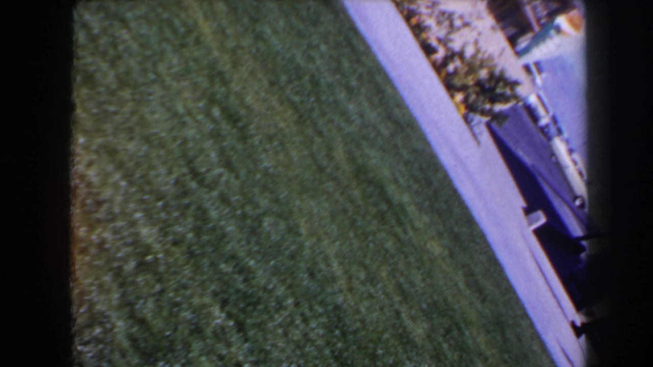 Tilted 1958 Las Vegas 8mm frame showing a lawn, sidewalk edge and partial roadside or curb area.
