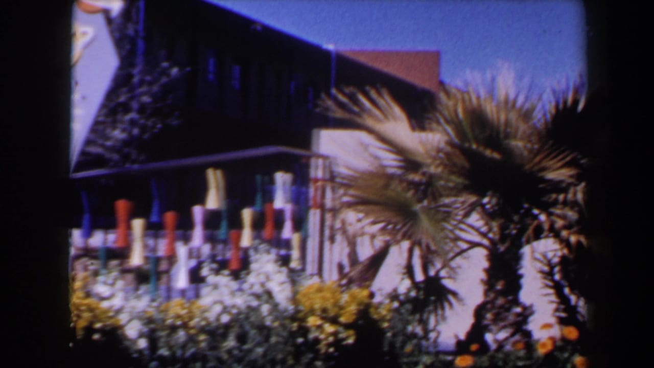1958 Las Vegas exterior with palm trees, a pale wall, low building roofline, flowers and colorful decorative posts.