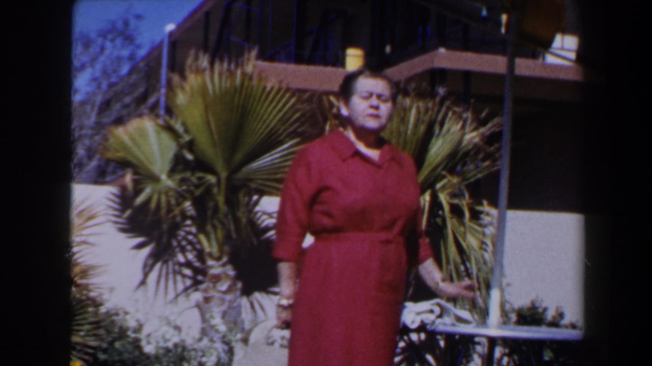 1958 Las Vegas home-movie frame of a mature woman in a red dress standing near a patio table with palms behind her.
