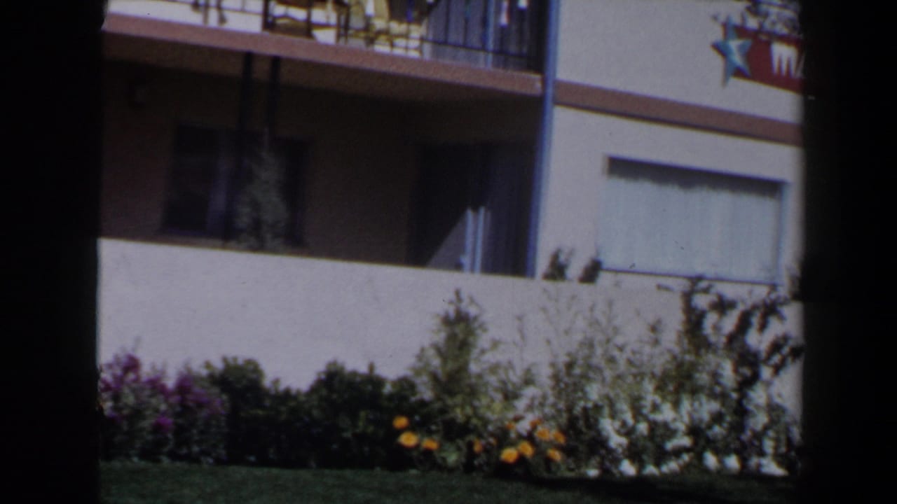 The camera view shifts to a low Las Vegas building facade with balcony railings, garden beds, and a partial sign near the upper edge.