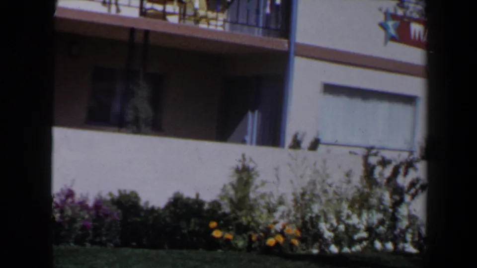 The camera view shifts to a low Las Vegas building facade with balcony railings, garden beds, and a partial sign near the upper edge.