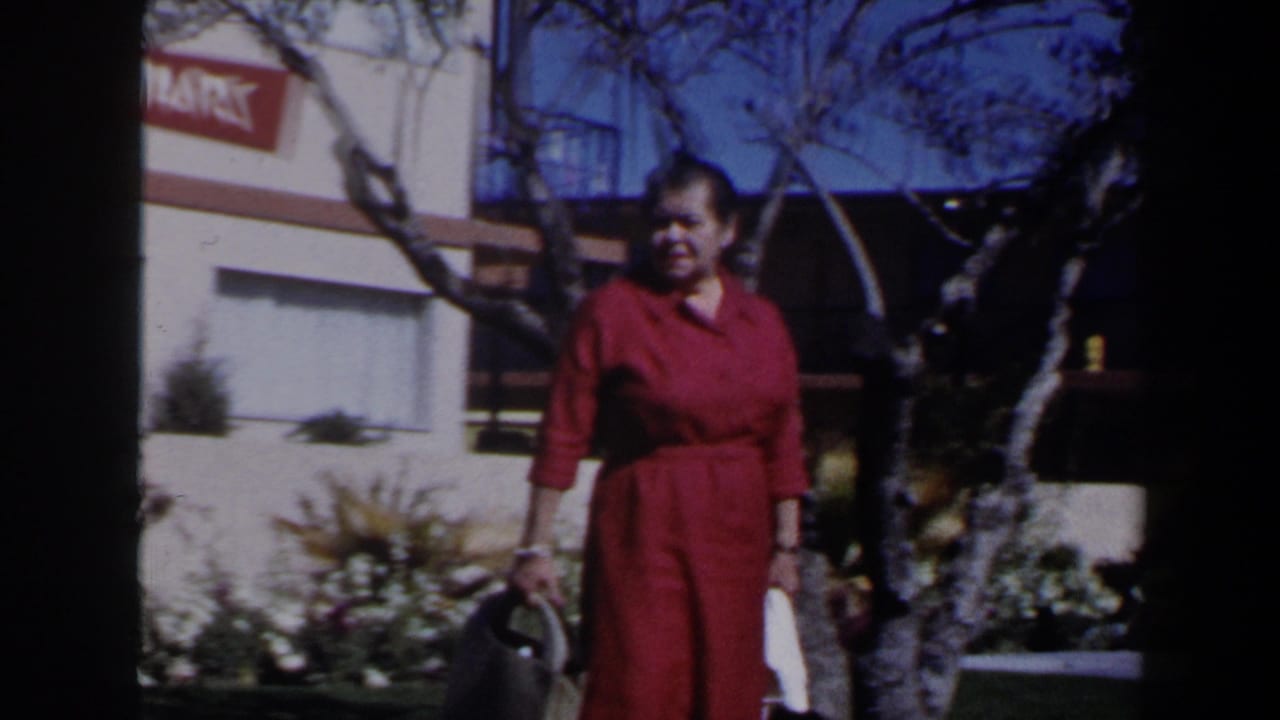 Woman in a red dress walking past a bare tree near a partial sign.