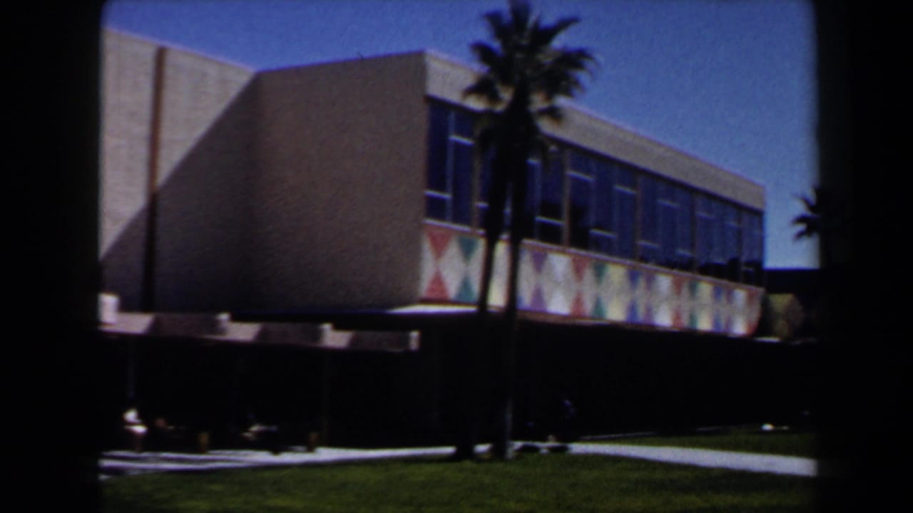 Las Vegas 1958 exterior view of a modern building with palm trees, trimmed lawn, and a colorful geometric band along the facade.