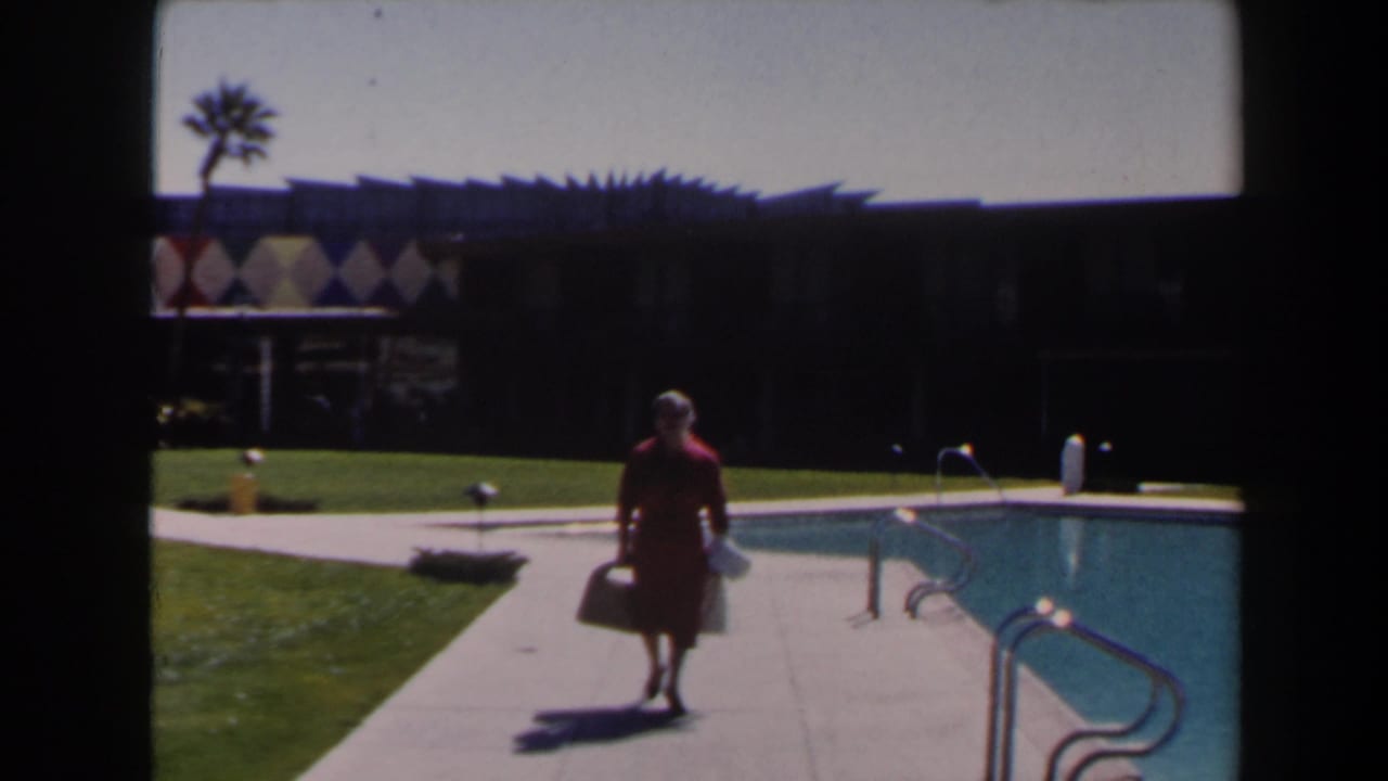 In Las Vegas 1958 footage, a woman in a red dress walks toward camera beside a blue swimming pool and low modern building.