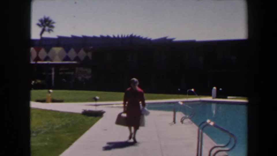 In Las Vegas 1958 footage, a woman in a red dress walks toward camera beside a blue swimming pool and low modern building.