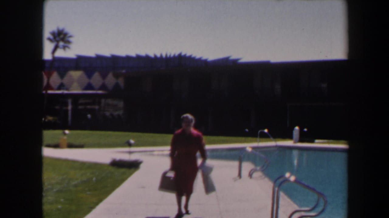 A woman in a red dress carries items along a Las Vegas poolside walkway, with lawn and a low building behind her.