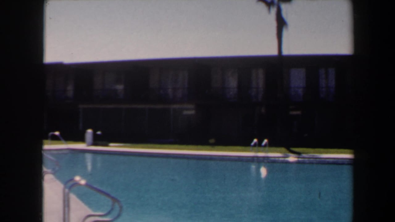 The final frame holds on the blue pool, metal ladders, palm trunk, and shaded low building in Las Vegas 1958 footage.