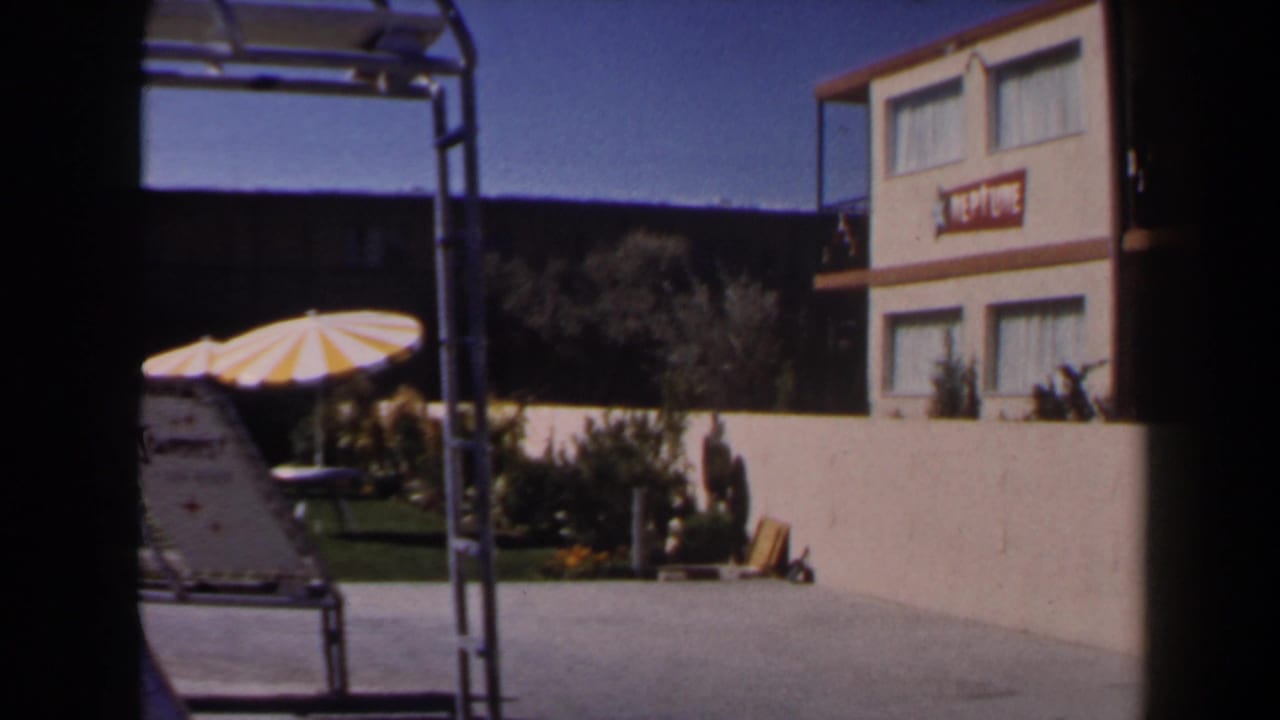 Hotel courtyard with striped umbrella, lounge chair, plants, and motel building signage.