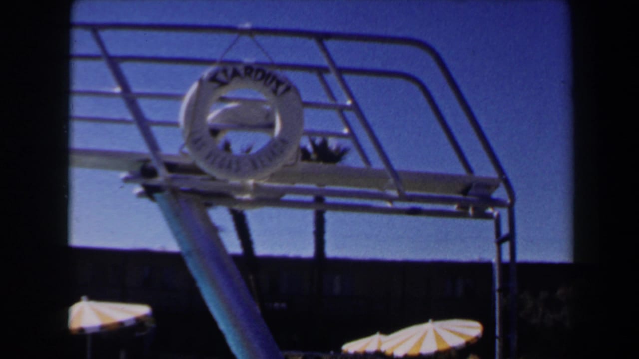 1958 Las Vegas poolside view with a Stardust life ring on a metal diving structure, striped parasols, and blue sky.