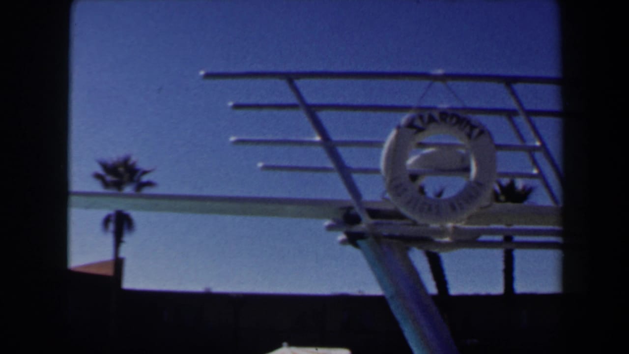 Las Vegas resort pool detail showing a Stardust life ring on a diving board frame, with a palm tree and clear sky behind.