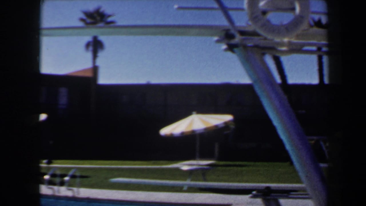1958 Las Vegas poolside frame with a striped umbrella, diving board structure, palm silhouettes, and dark motel-like facade.