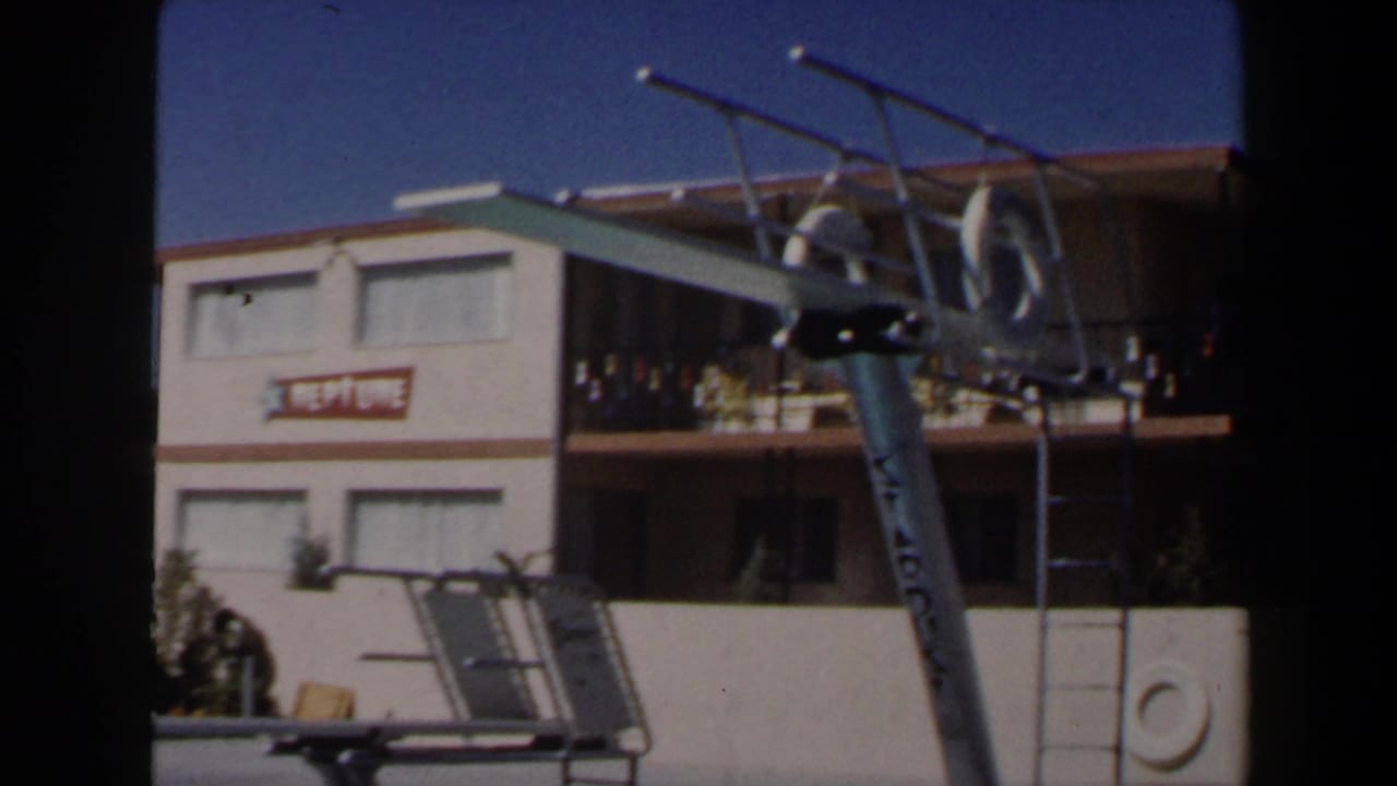 1958 Las Vegas motel pool frame showing the NEPTUNE sign, balcony railings, silver diving board, and poolside ladder.
