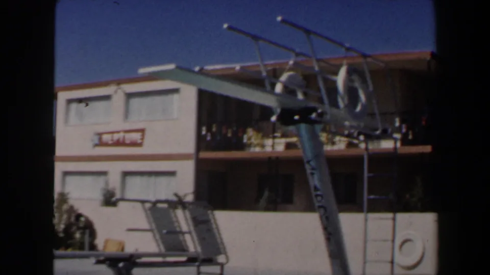 1958 Las Vegas motel pool frame showing the NEPTUNE sign, balcony railings, silver diving board, and poolside ladder.