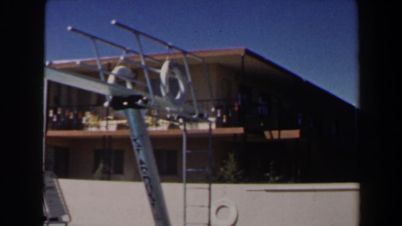 1958 Las Vegas home-movie frame with a silver diving board in the foreground and a two-story motel balcony behind it.