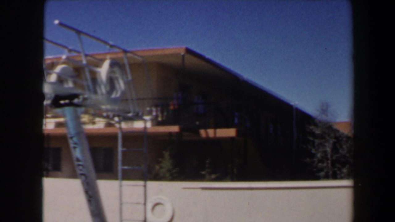 1958 Las Vegas home-movie frame showing a motel exterior, balcony, pool ladder, white wall, and clear blue sky.