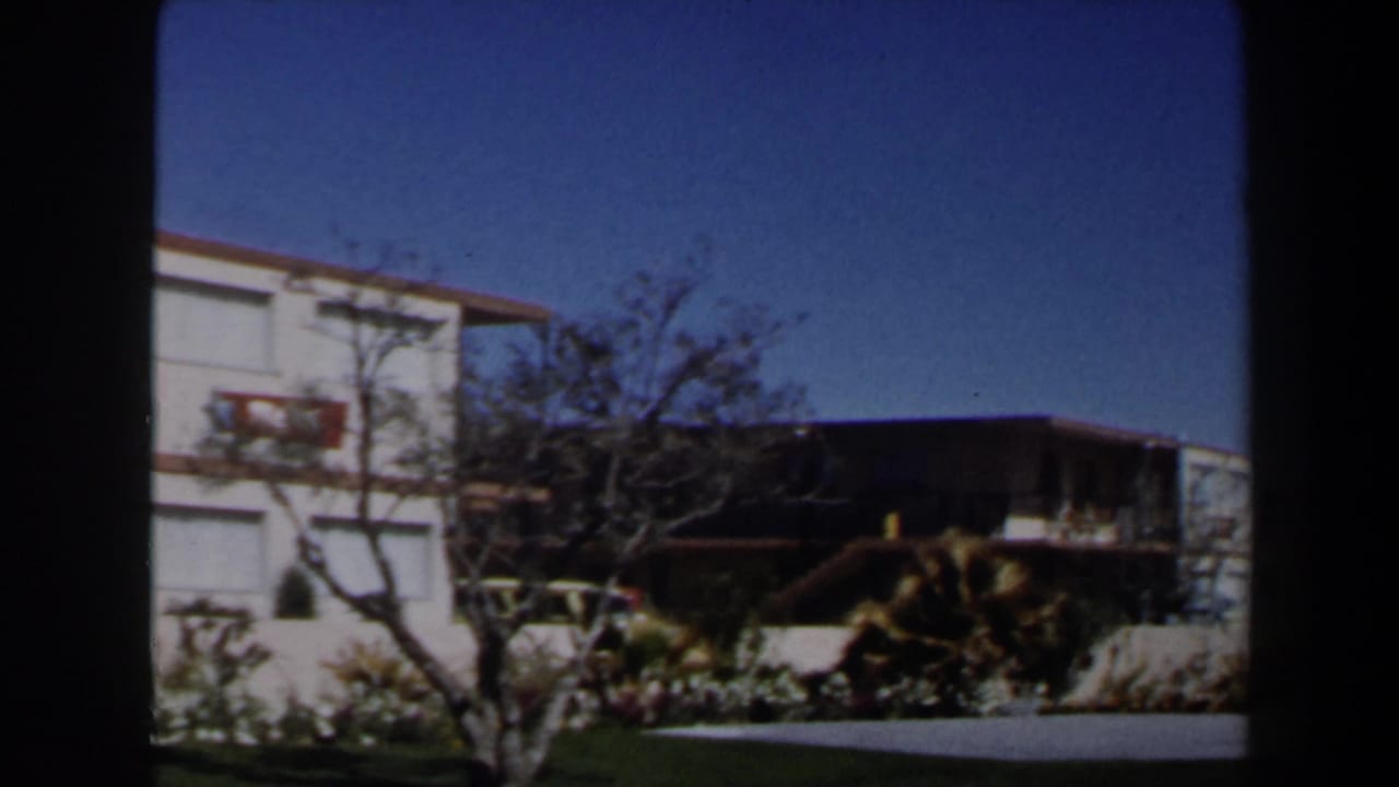 1958 Las Vegas residential exterior with stucco walls, balcony railing, small tree, planted shrubs, and a sunlit driveway area.