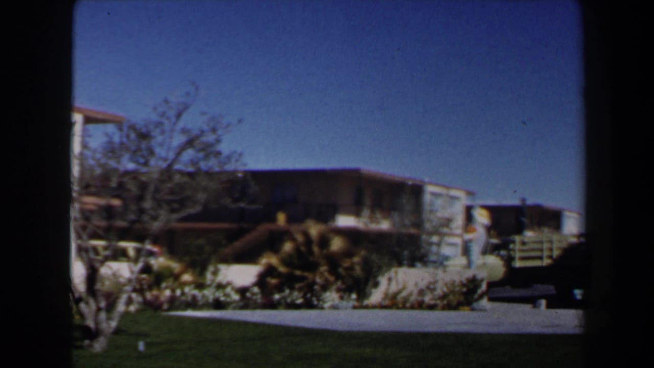 1958 Las Vegas home-movie view of a landscaped lawn, small tree, low wall, and flat-roofed residential building in the background.