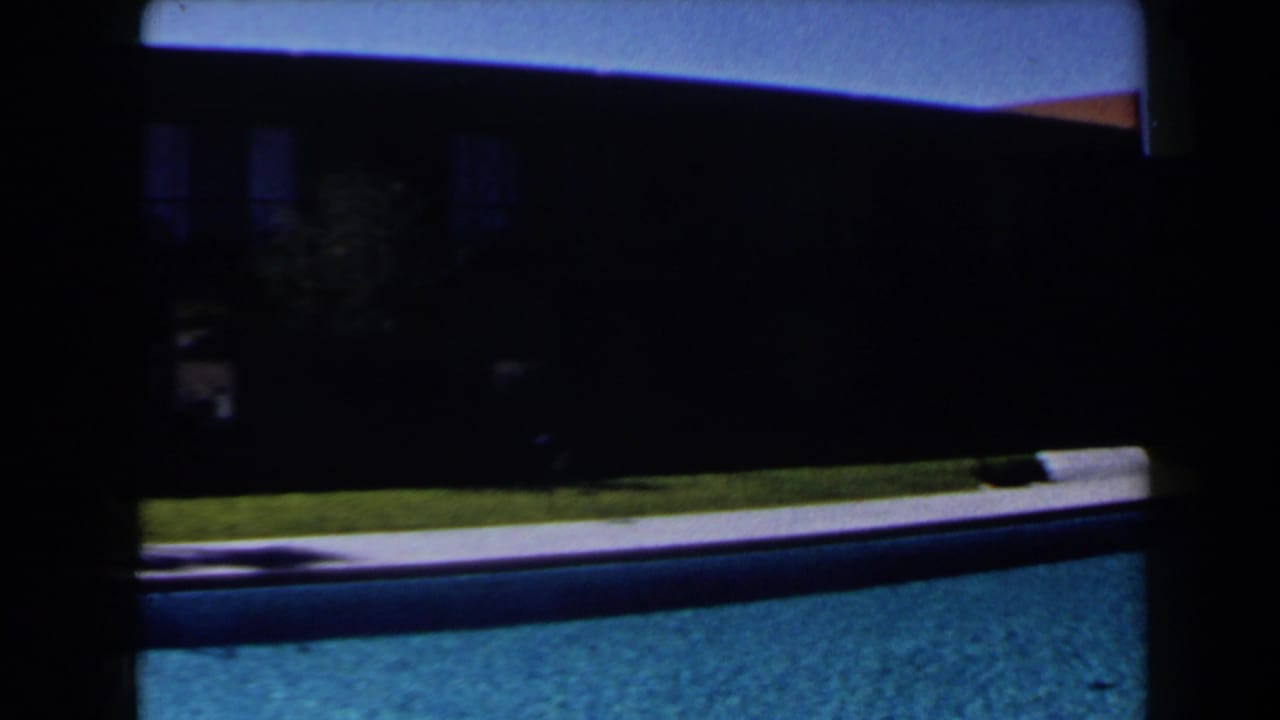 Blue pool in foreground with shaded brown building and lawn behind it.