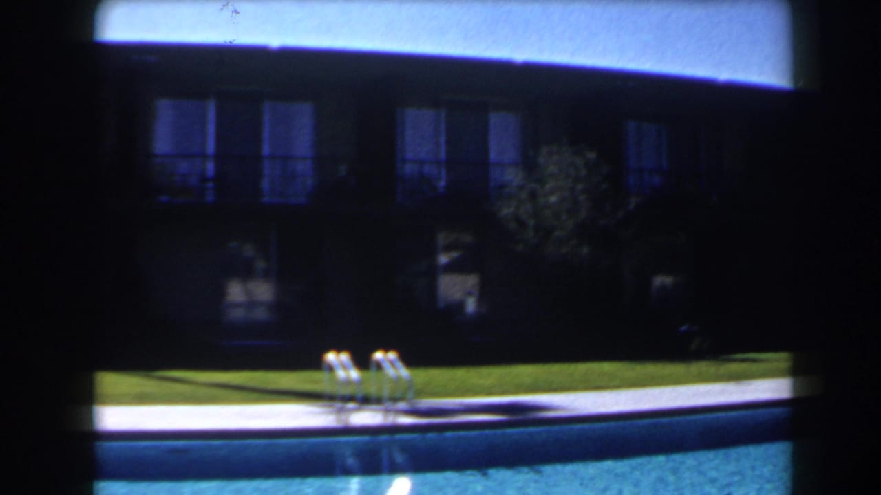 1958 Las Vegas frame with a metal pool ladder, blue water, lawn, and shaded motel balconies in the background.