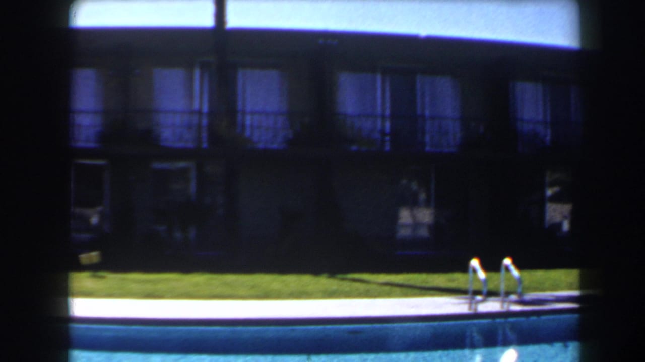 1958 Las Vegas poolside frame showing blue water, a white pool edge, green lawn, and a shaded two-story building.