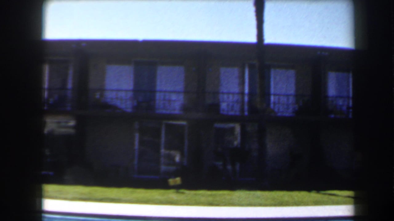 1958 Las Vegas home-movie frame of a shaded motel-style exterior beyond a lawn and bright pool edge.