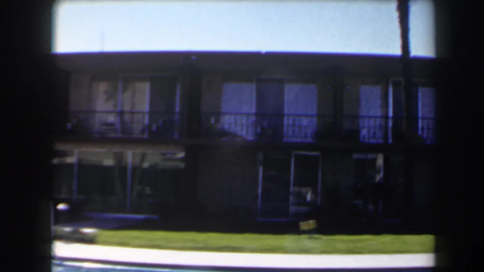 1958 Las Vegas 8mm frame showing a two-story lodging or apartment exterior beyond a lawn and swimming pool edge.