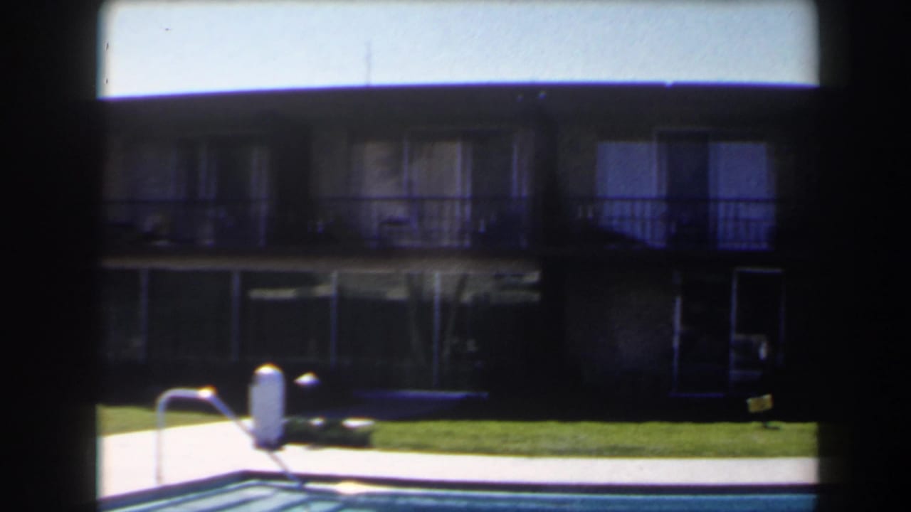 1958 Las Vegas roadside frame with a pool ladder, green lawn, and mid-century two-story exterior in the background.