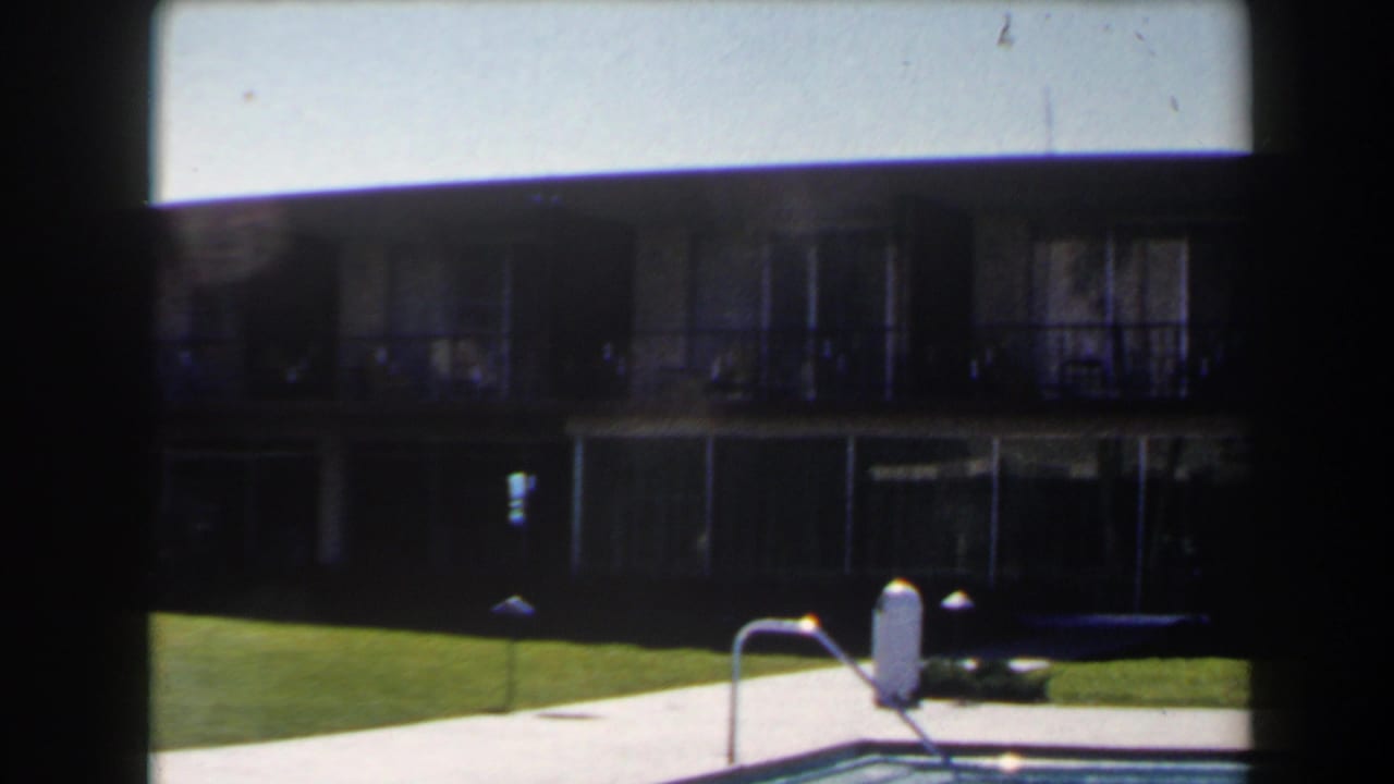 1958 Las Vegas 8mm frame with darker exposure on a poolside lawn, walkway, lamps, and two-story exterior.