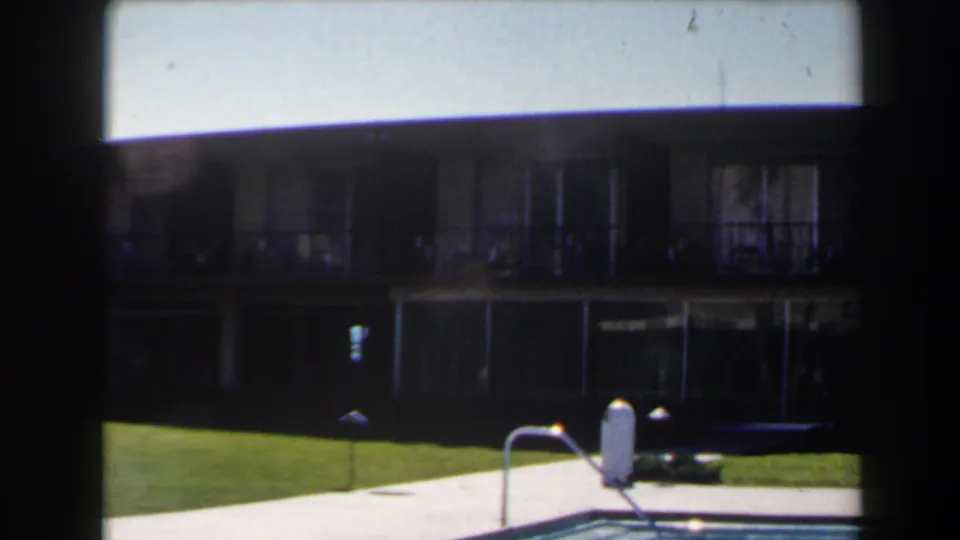 1958 Las Vegas 8mm frame with darker exposure on a poolside lawn, walkway, lamps, and two-story exterior.