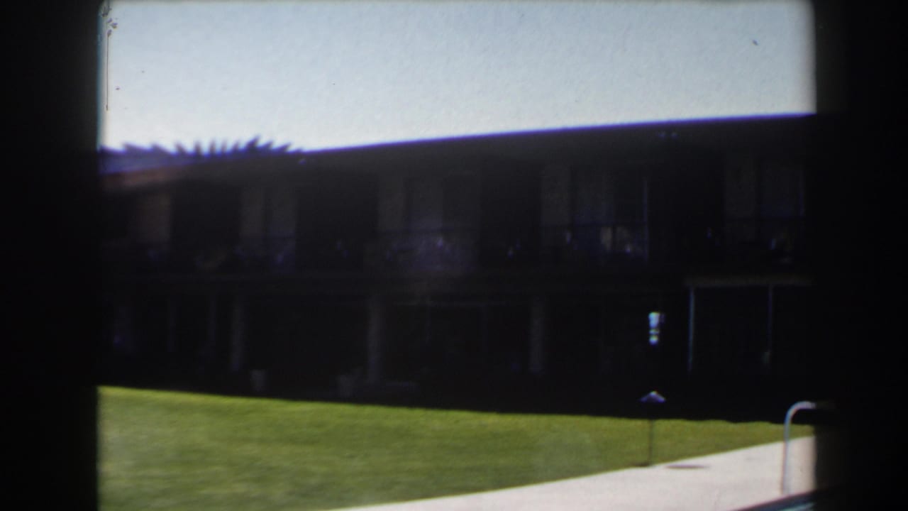 Final 1958 Las Vegas frame showing a lawn and pool edge with the shadowed building exterior receding at right.