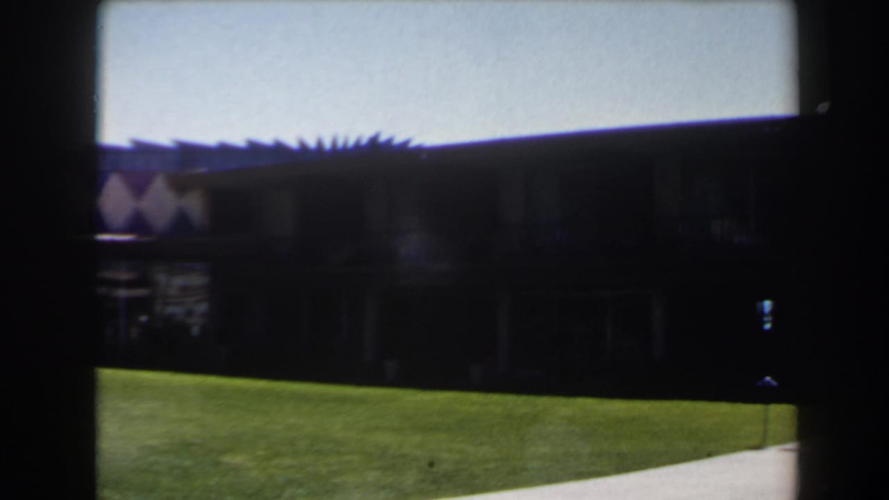 1958 Las Vegas home-movie frame showing a low colorful building, lawn, blue sky, and heavy film-edge shadowing.