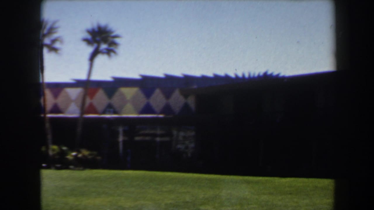 1958 Las Vegas frame with two palms, a colorful diamond facade, shaded lower level, and bright grass in the foreground.