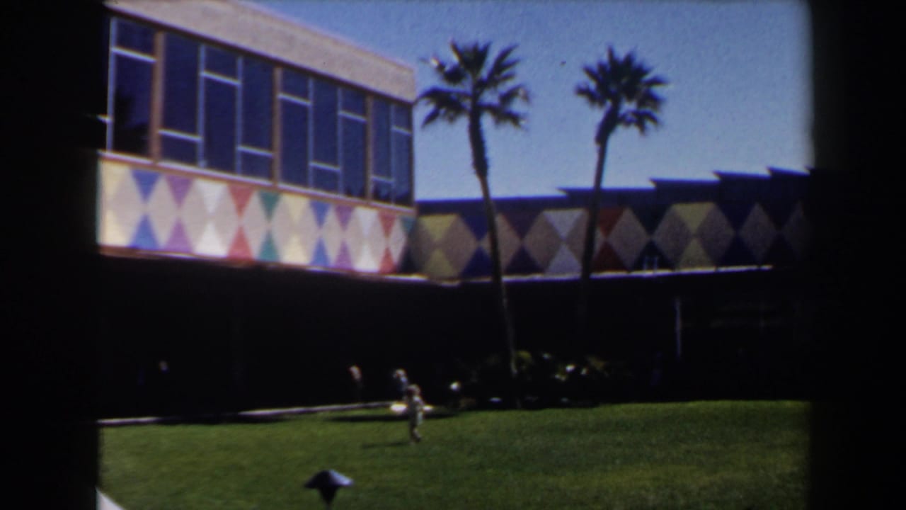 1958 Las Vegas home-movie frame showing people on a lawn, palms, upper windows, and a multicolor diamond facade.