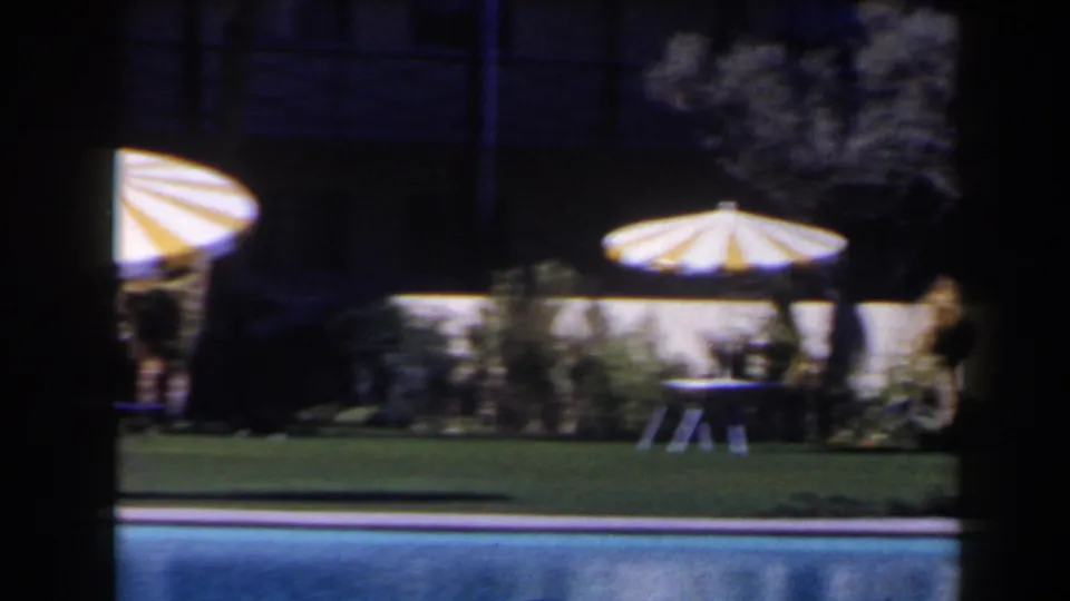 1958 Las Vegas resort poolside view with yellow-and-white striped parasols, lawn, tables and shrubs beyond the pool.