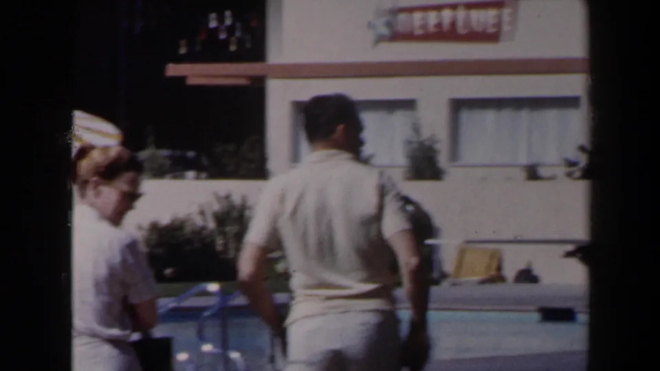 1958 Las Vegas resort poolside frame with adult guests, lounge chairs and a hotel building bearing a visible NEPTUNE sign.